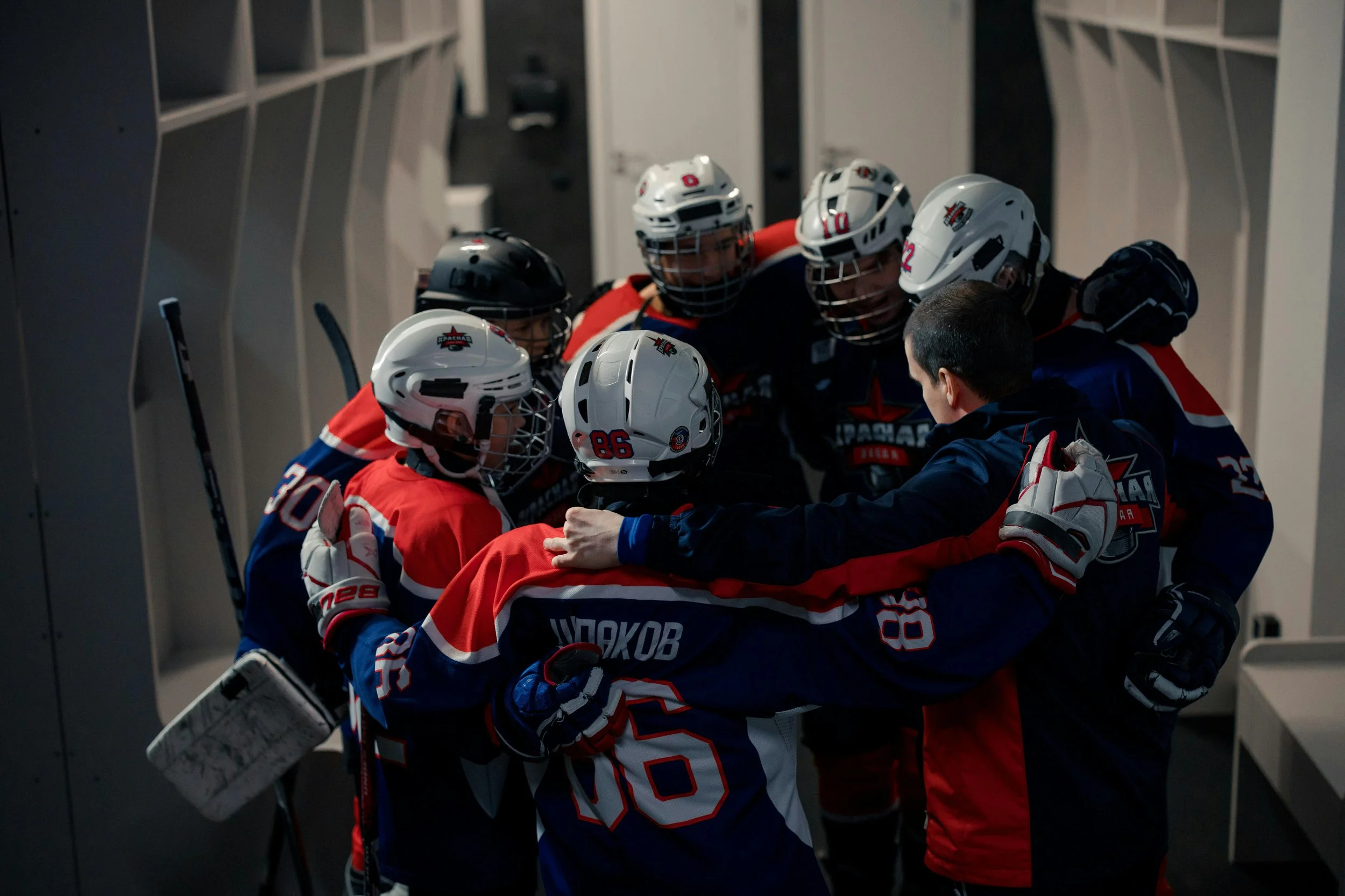 Hockey players in a locker room huddled around their coach during a team meeting.