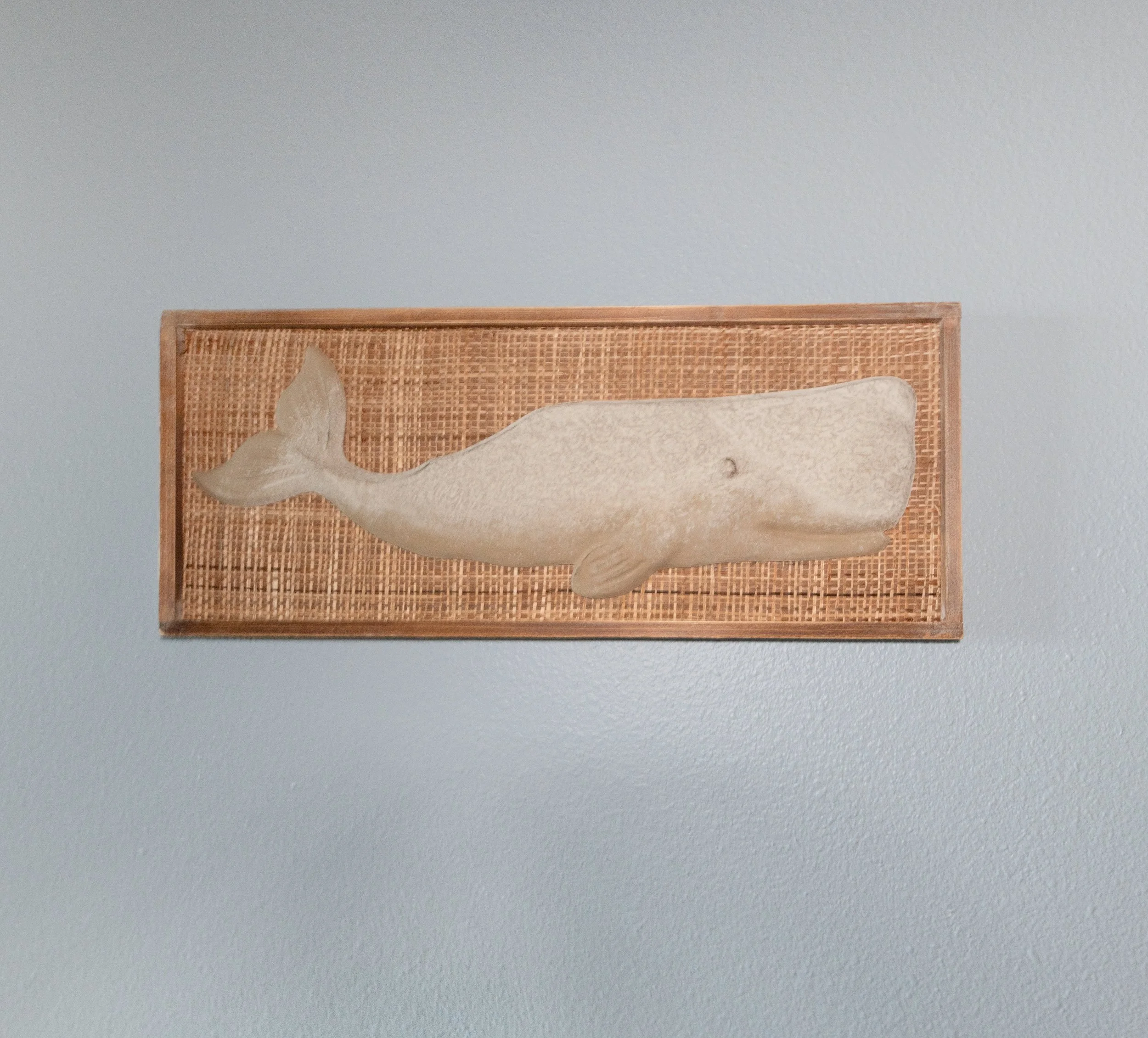 A framed artwork of a whale carving mounted on a gray wall.