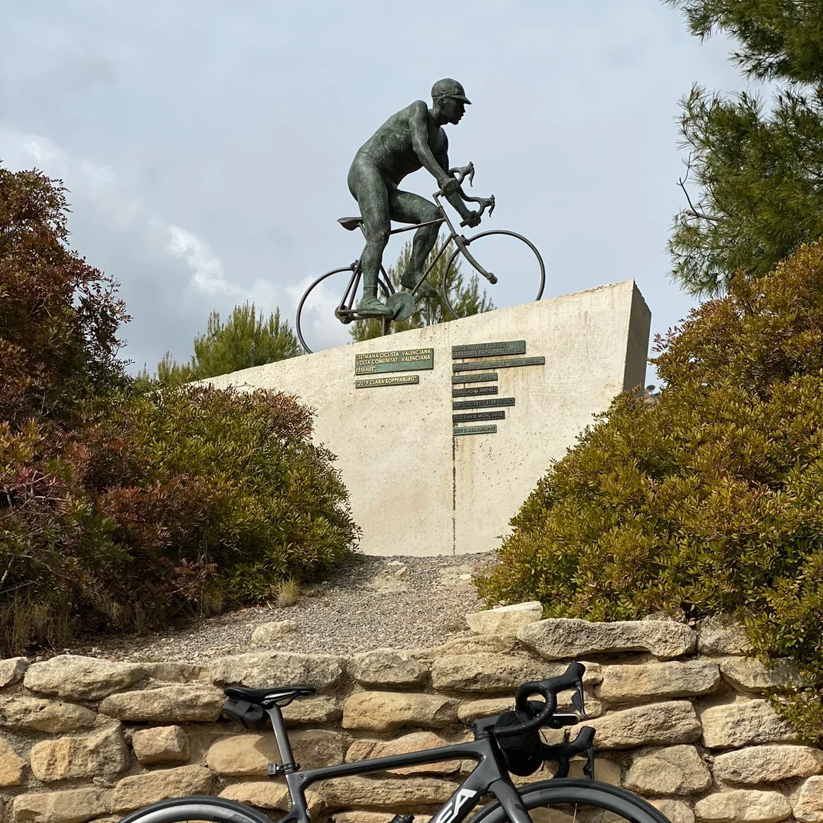 A statue of a cyclist on top of a cement base among trees