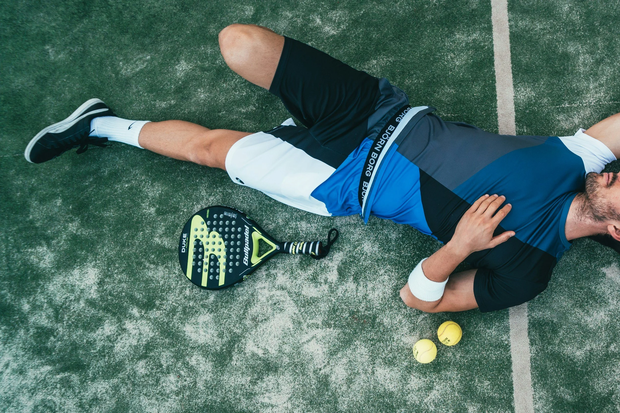 a man lying exhausted on a padel court with a padel racket by his side