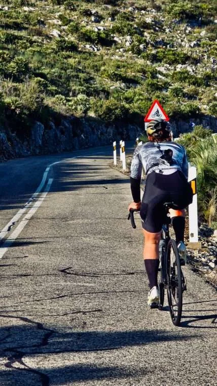 A bike rider ascending a paved road towards a curve