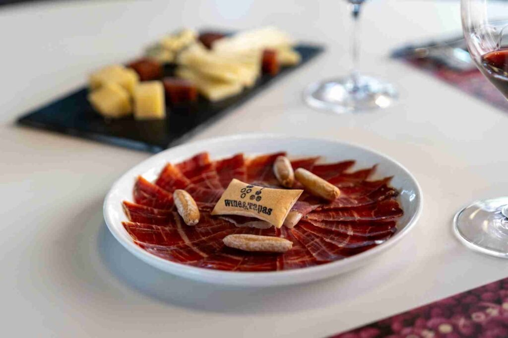 A plate of cured ham with cheese in the background served at Wine & Tapas restaurant in Oliva Nova