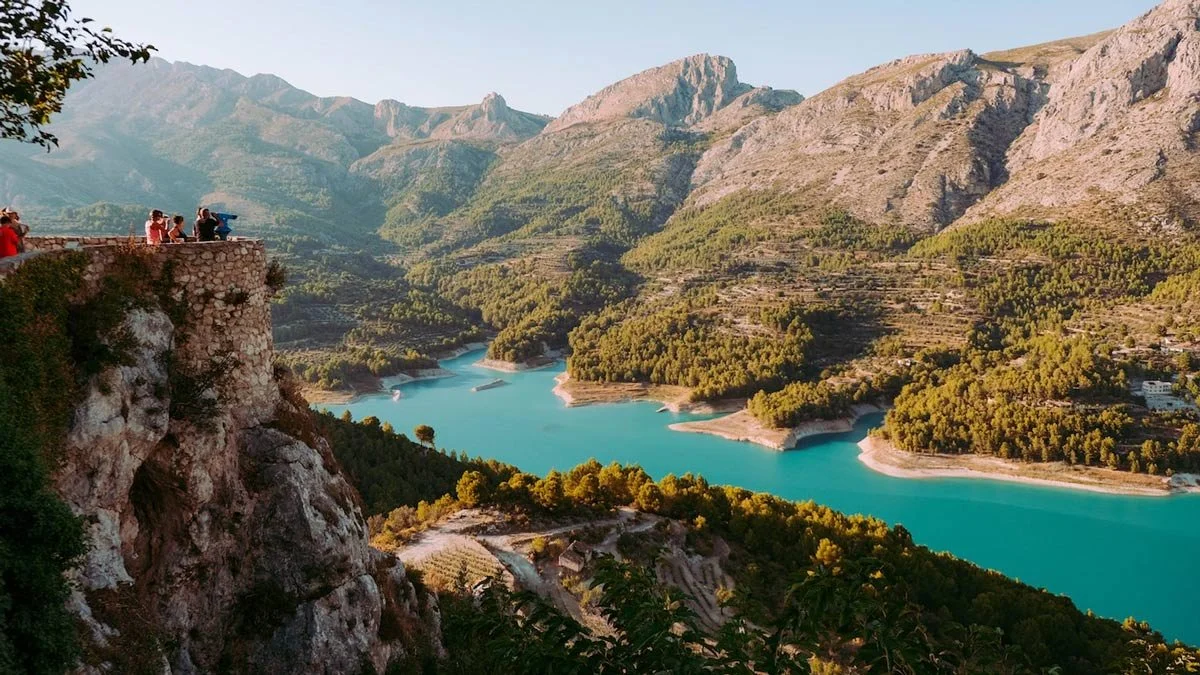 A turquoise lake at the bottom of the valley with a castle in front and mountains behind