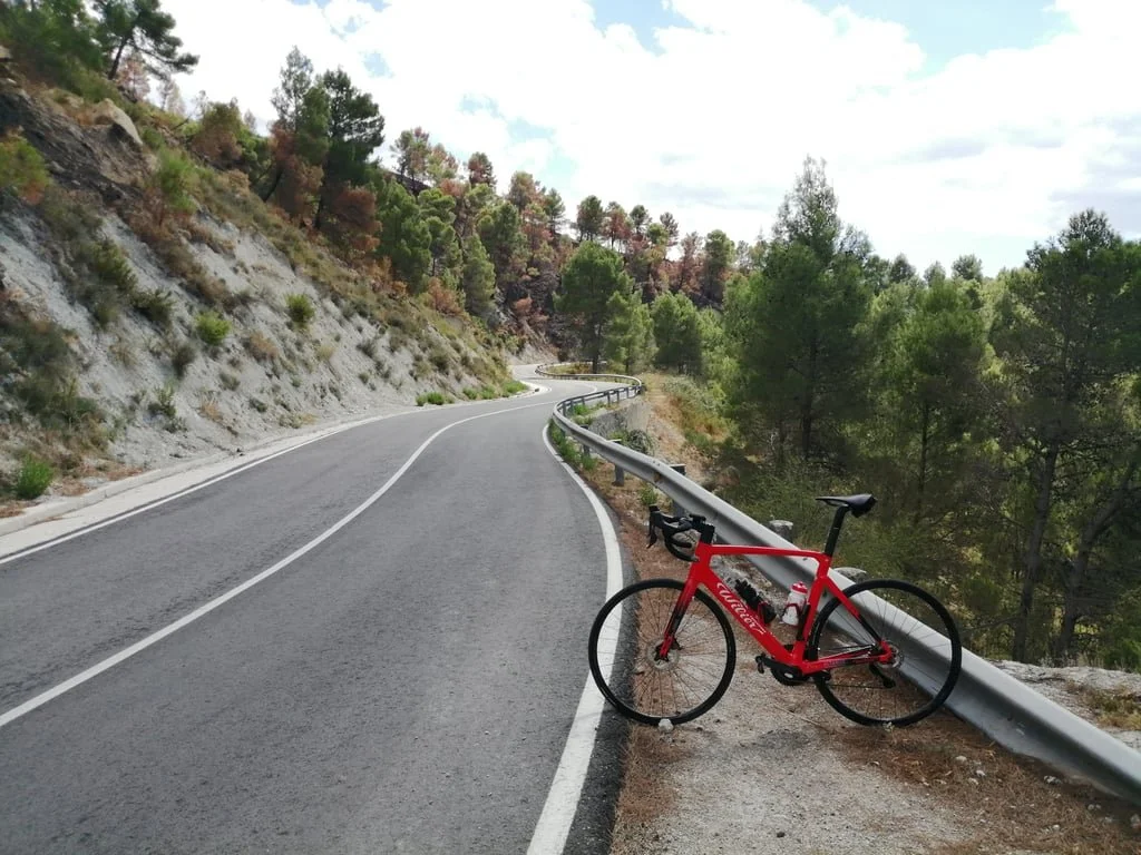 A red road bike parked on the side of a paved road winding up a valley