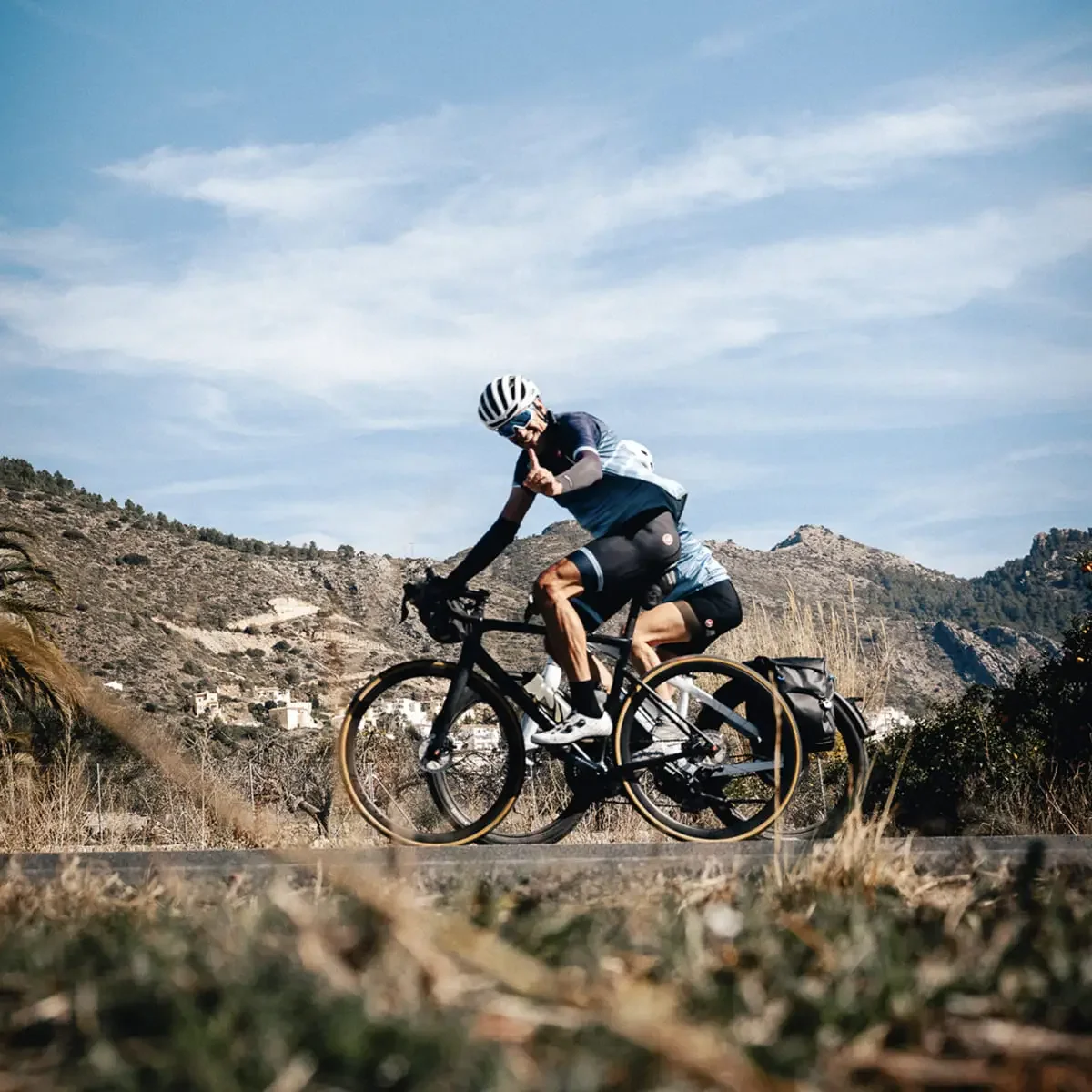 A cyclist on a roadbike giving thumbs up with a mountain in the background