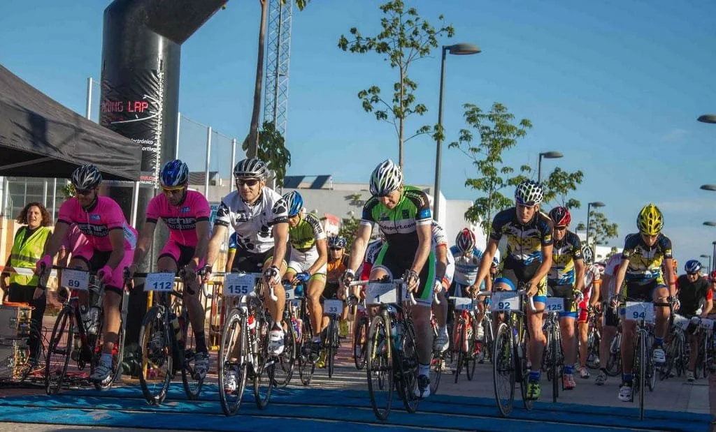 Cyclists in multicolored uniforms starting out on a bicycle race underneath and arc with trees in the background