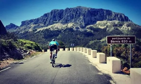 A man cycling on a paved road starting the descent from Sierra de Bernia with the mountain in the background