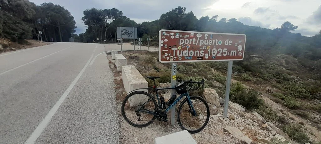 A bicycle is parked on the side of the road in front of the sign for port de tudons