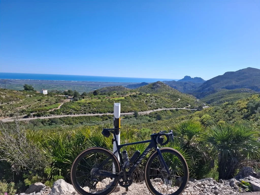 A bike parked on a roadside overlooking a mountaineous valley with the sea in the background
