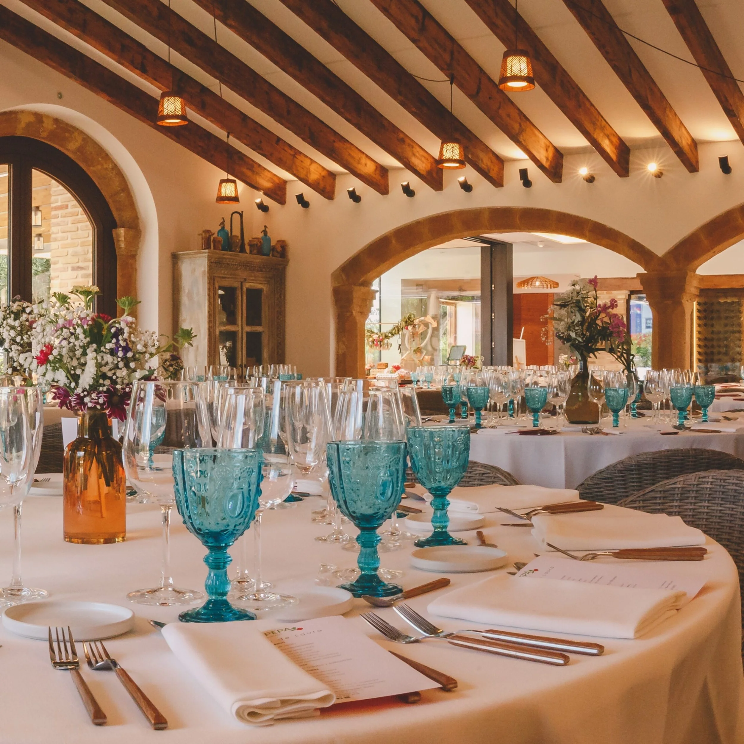 A set table with white linen and turquoise glases in the dining room of Casa Pepa restaurant in Ondara