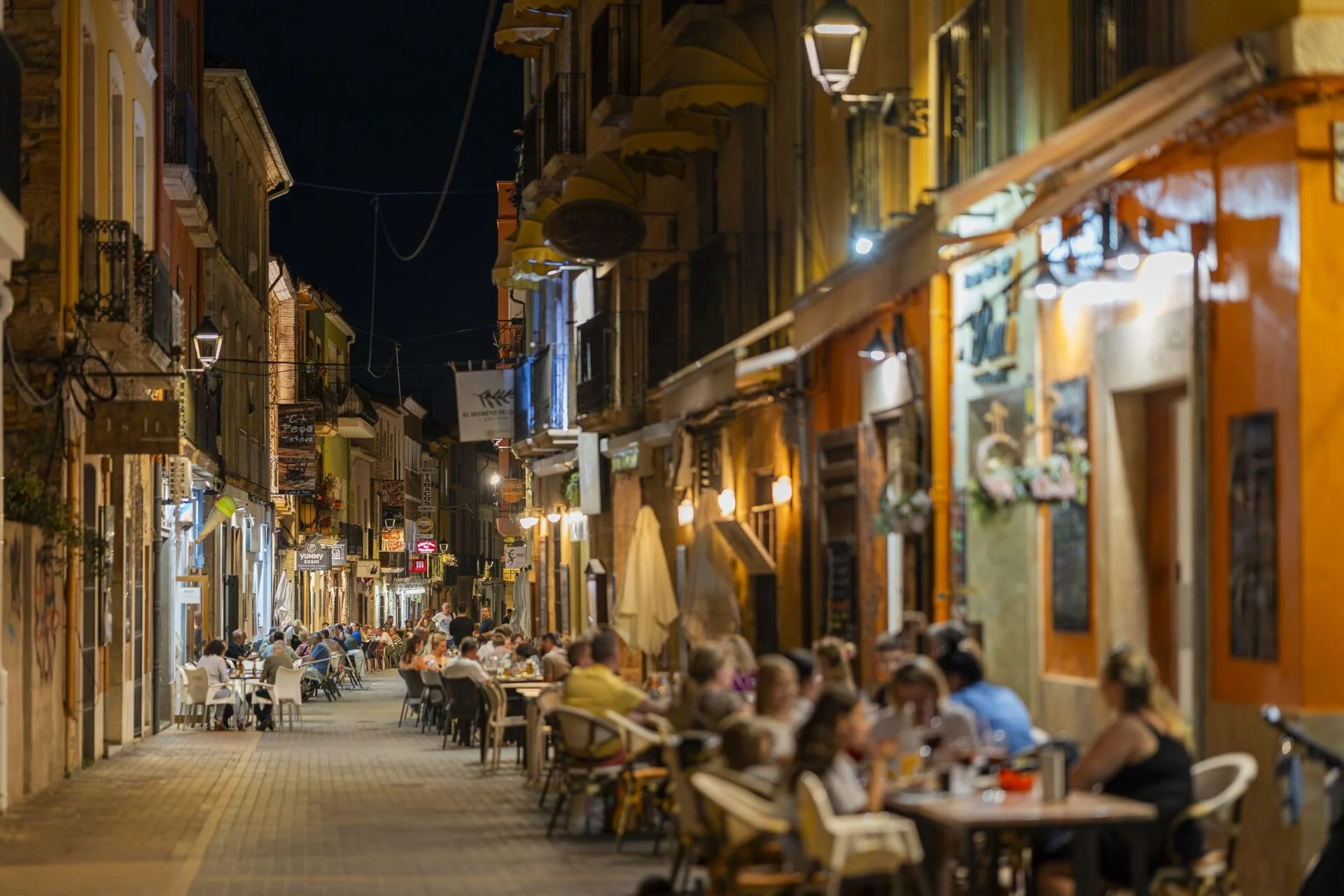 A night-time view showing many people sitting at outside restaurant tables in Calle Loreto, Dénia