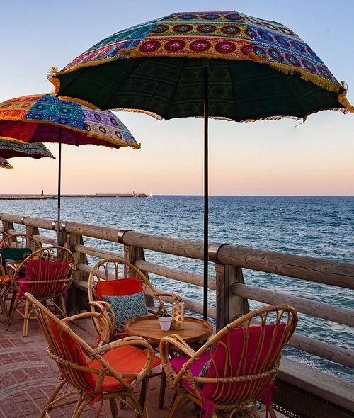 A colorful parasol shield wood lounge table and chairs with the sea in the background