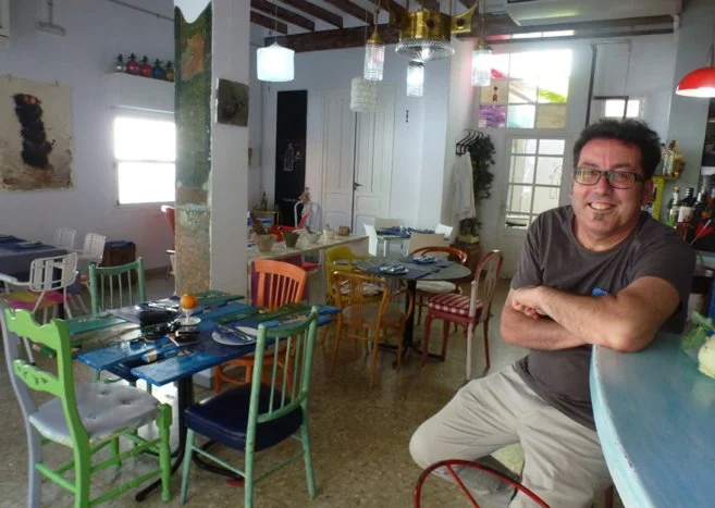 The chef Miquel Ruiz in his restaurant El Baret de Miquel at the bar in front of set tables with colorful chairs