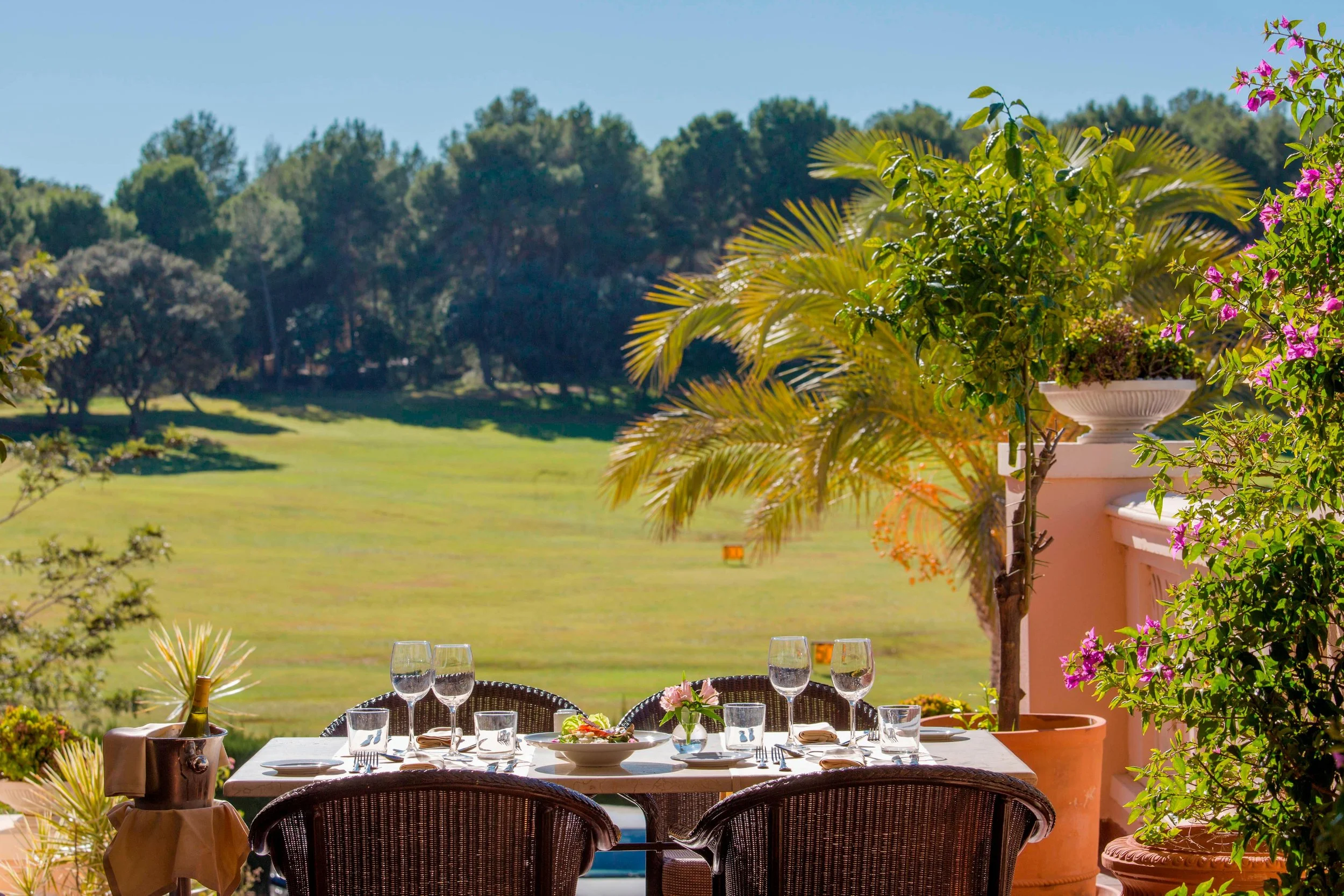 A set table on an outdoor terrace overlooking a green field and a forest at Montgó restaurant at Dénia Marriott La Sella Hotel