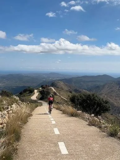 A cyclist on a biking path on a mountain ridge with blue skies, clouds and the sea in the background