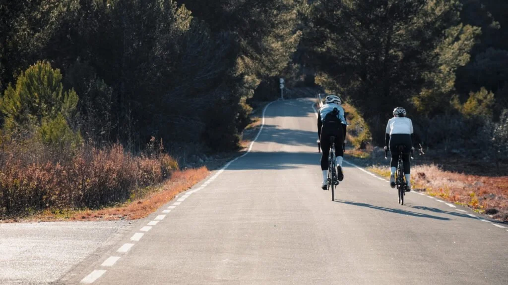 Two bike riders cycling on a paved road in a forest
