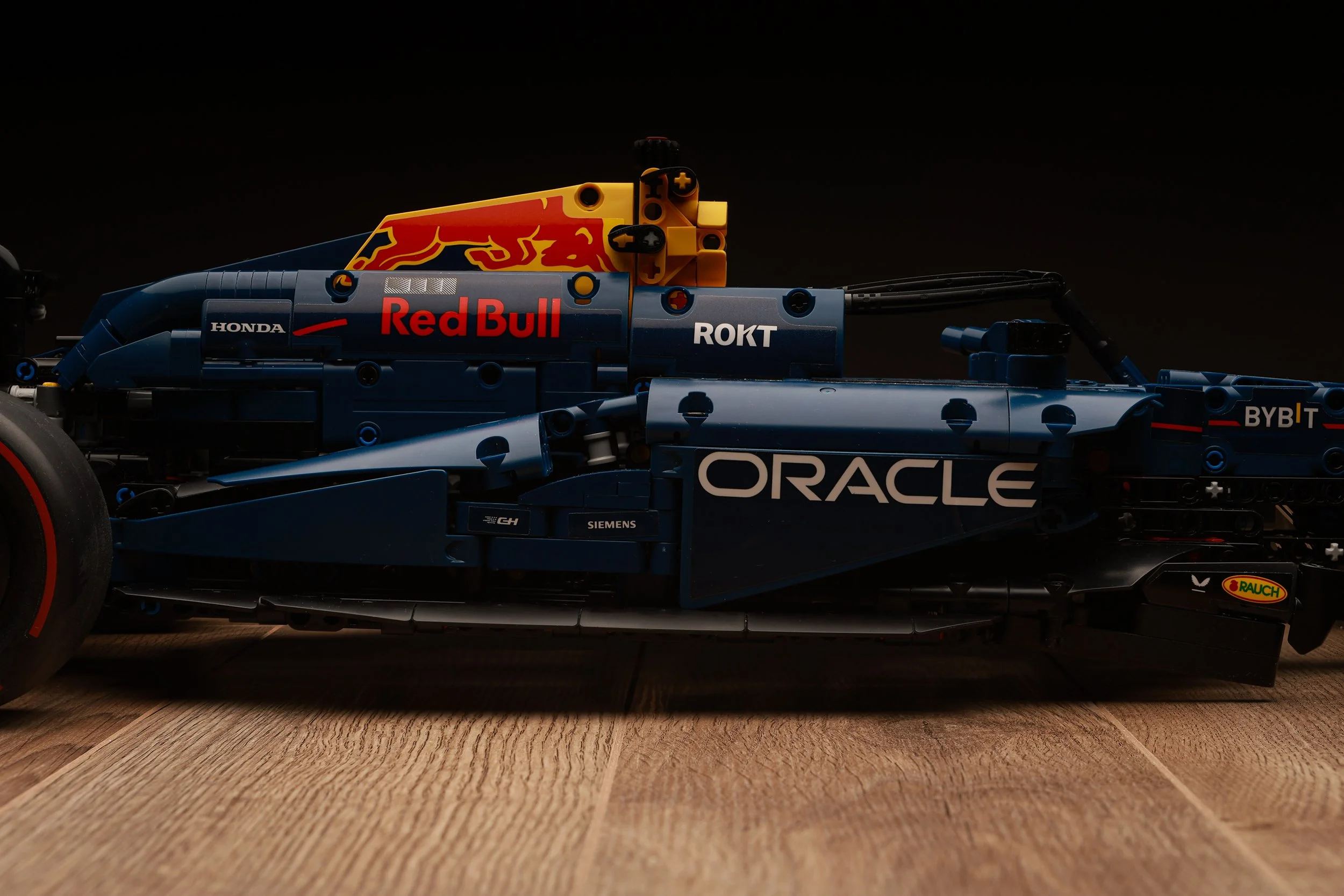 Modèle réduit de voiture de course de formule 1 avec logos de sponsors comme Oracle, Red Bull, Honda, et autres, placé sur un sol en bois.