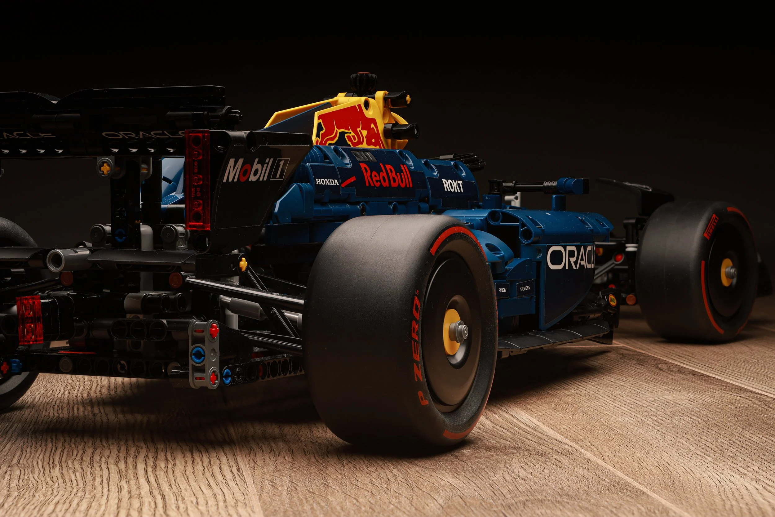 Modèle de voiture de course Red Bull Racing, avec des sponsors Mobil 1, Honda, Oracle, et P Zero sur les pneus, placé sur un sol en bois.