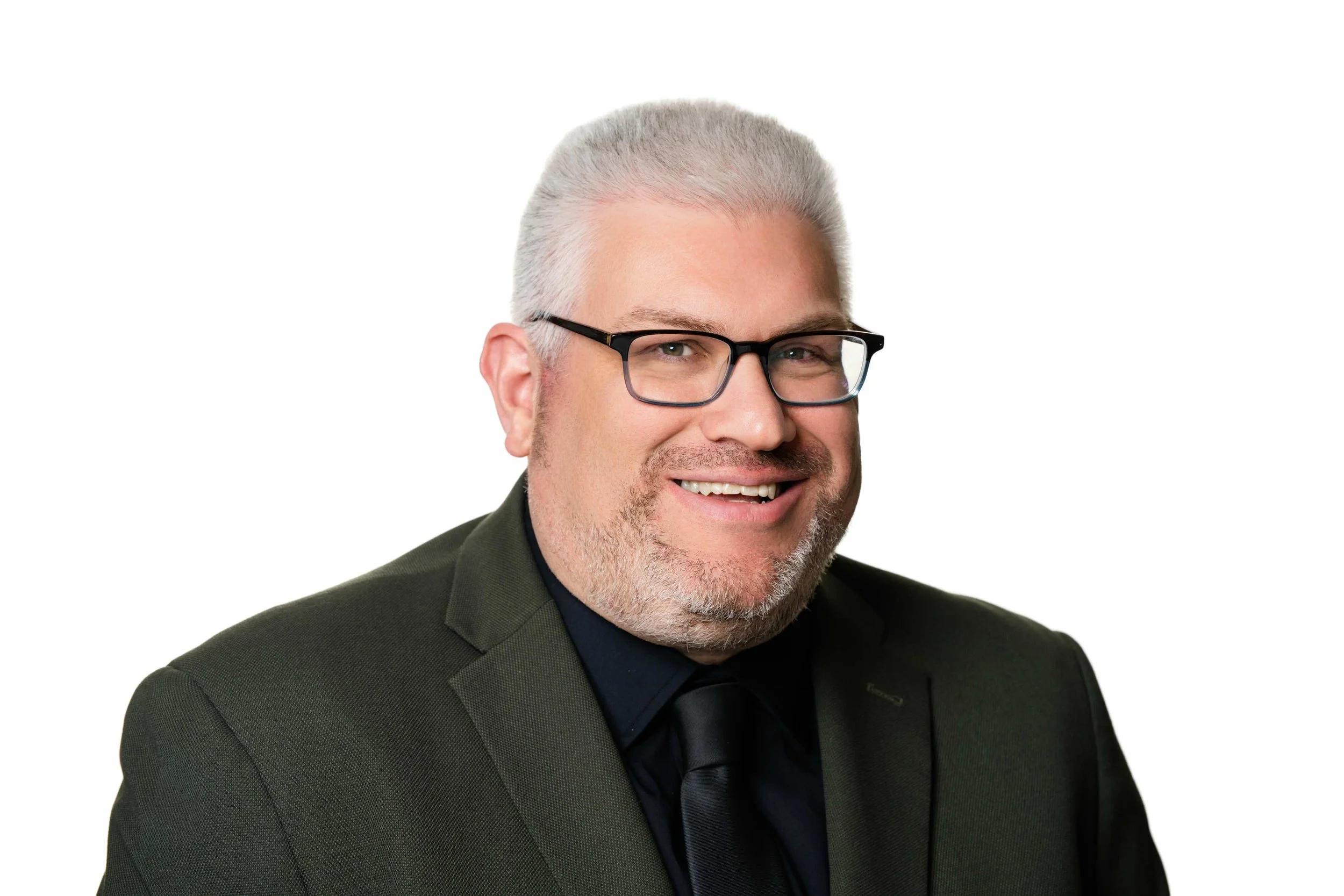 A smiling man with gray hair, wearing glasses, a dark green suit, black shirt, and black tie, against a white background.