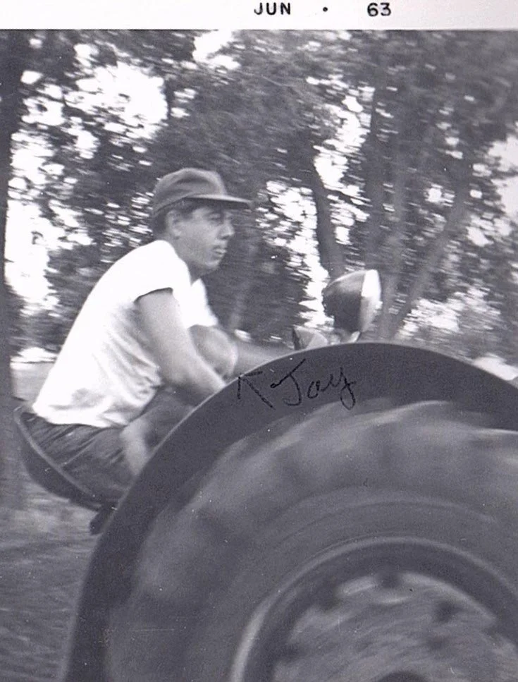 A young man riding a motorcycle outdoors, wearing a white shirt and a cap, with trees in the background. The photo is in black and white, dated June 1963, and has a handwritten signature that appears to say "K. Jay".