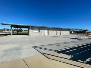 Empty outdoor area with a small building, parking lot, and a clear blue sky.