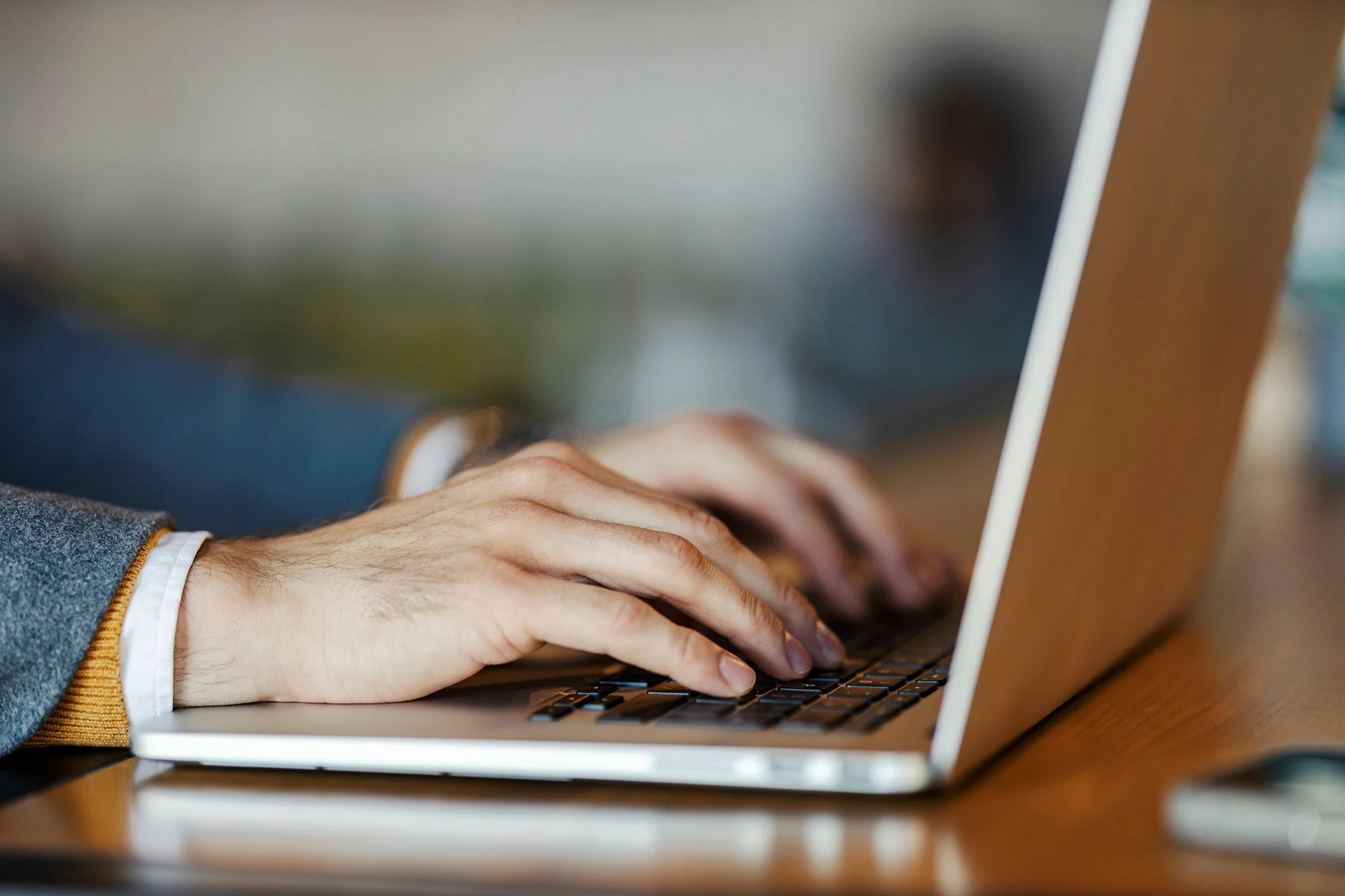 Close-up of person typing on a laptop keyboard at a wooden desk.