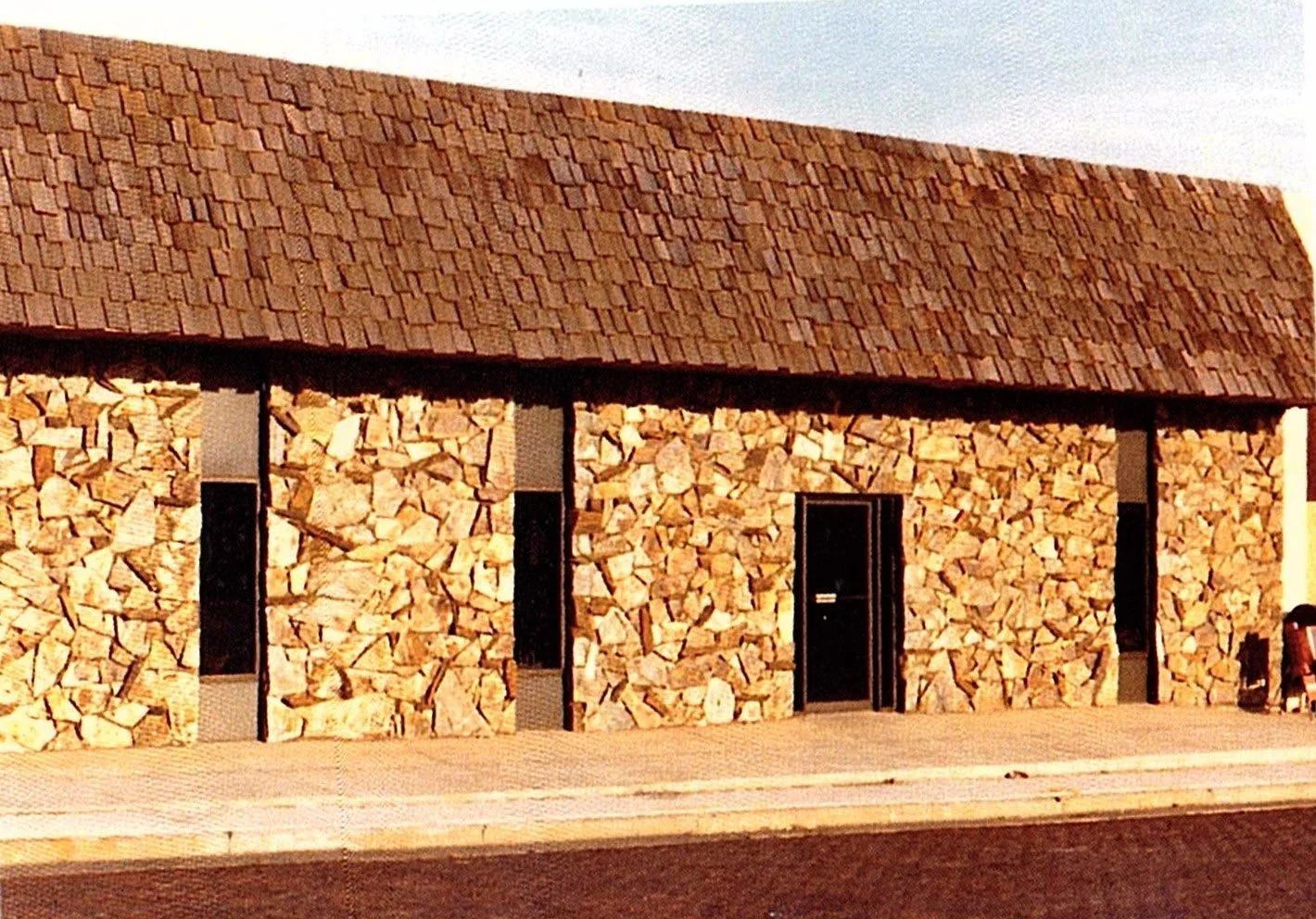 Exterior of a building with walls made of stacked firewood and a pitched shingle roof.