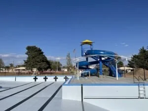 Empty outdoor swimming pool with multiple water slides and a clear blue sky above.