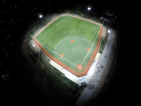A baseball field at night with tall floodlights illuminating the field.