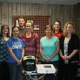 Group of people standing behind a table with school supplies, smiling in a classroom or community center.