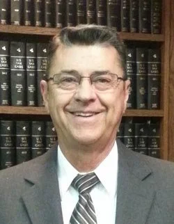 A man in a suit and tie smiling in front of a bookshelf filled with legal books.