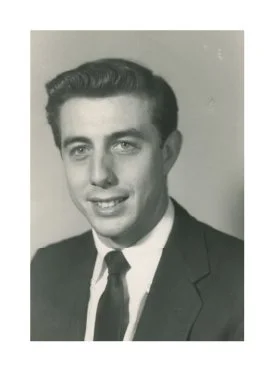 Black and white portrait of a young man in a suit and tie, smiling.