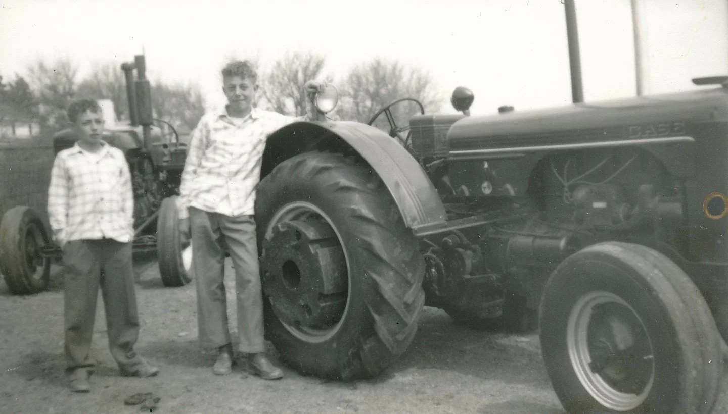 Two boys standing next to a vintage Case tractor outdoors, in black and white.