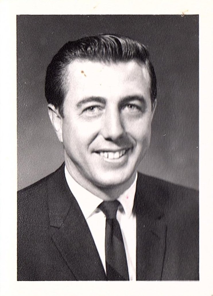 Black and white portrait of a man in a suit and tie, smiling slightly.