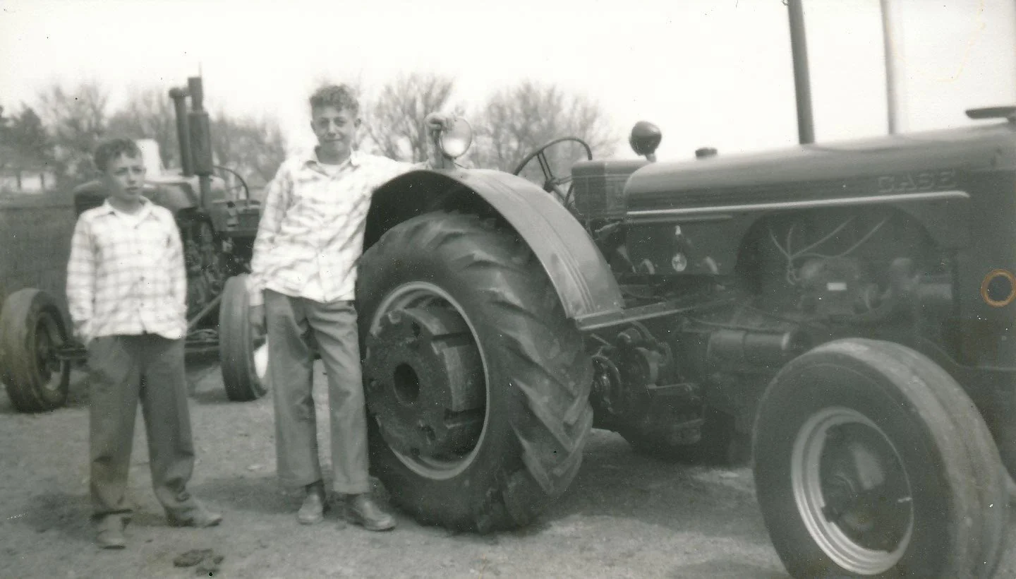 Two boys standing next to an old tractor in a field, black and white photograph.