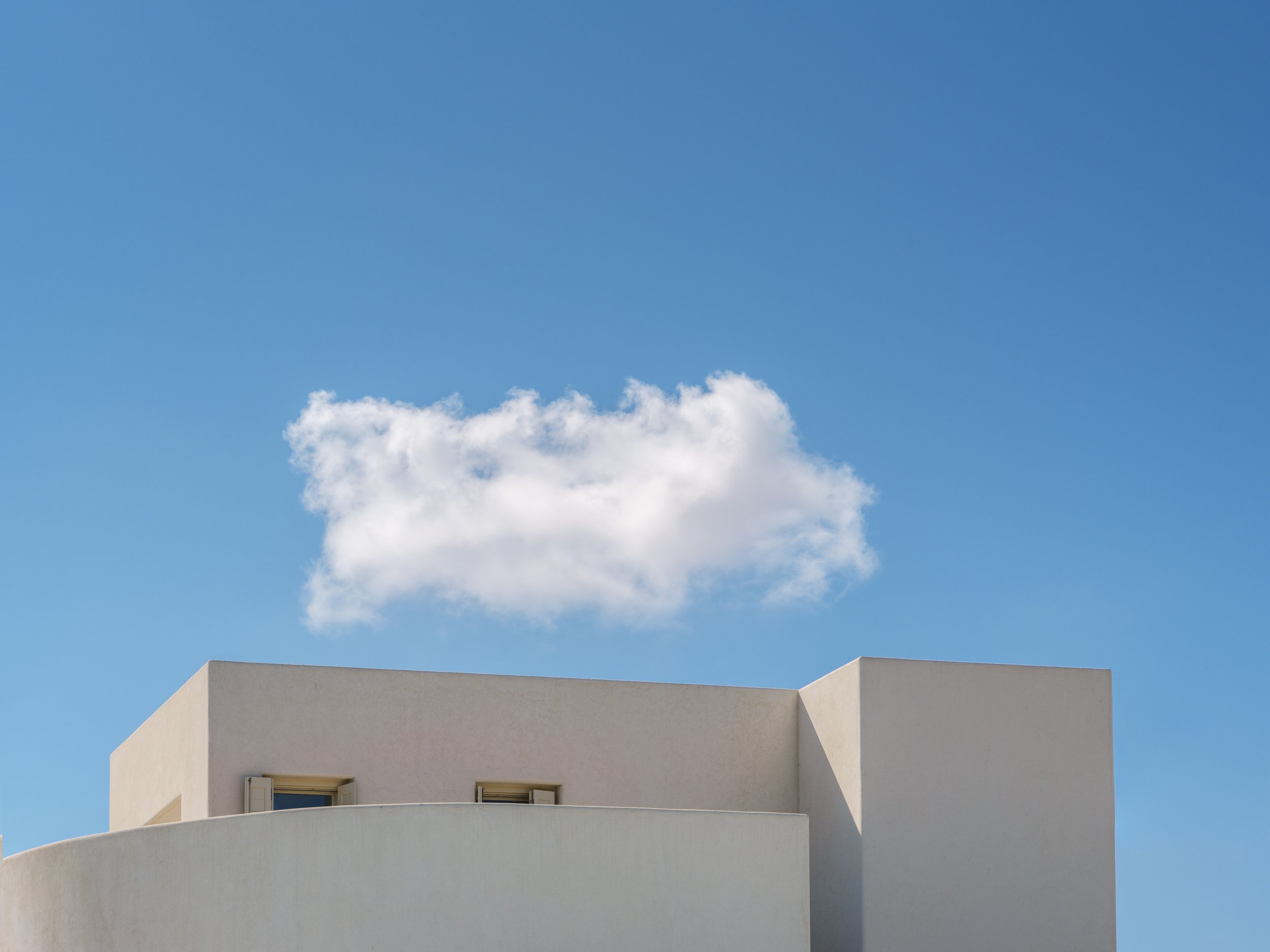 Modern white building with curved architectural design under a bright blue sky with a single fluffy white cloud.