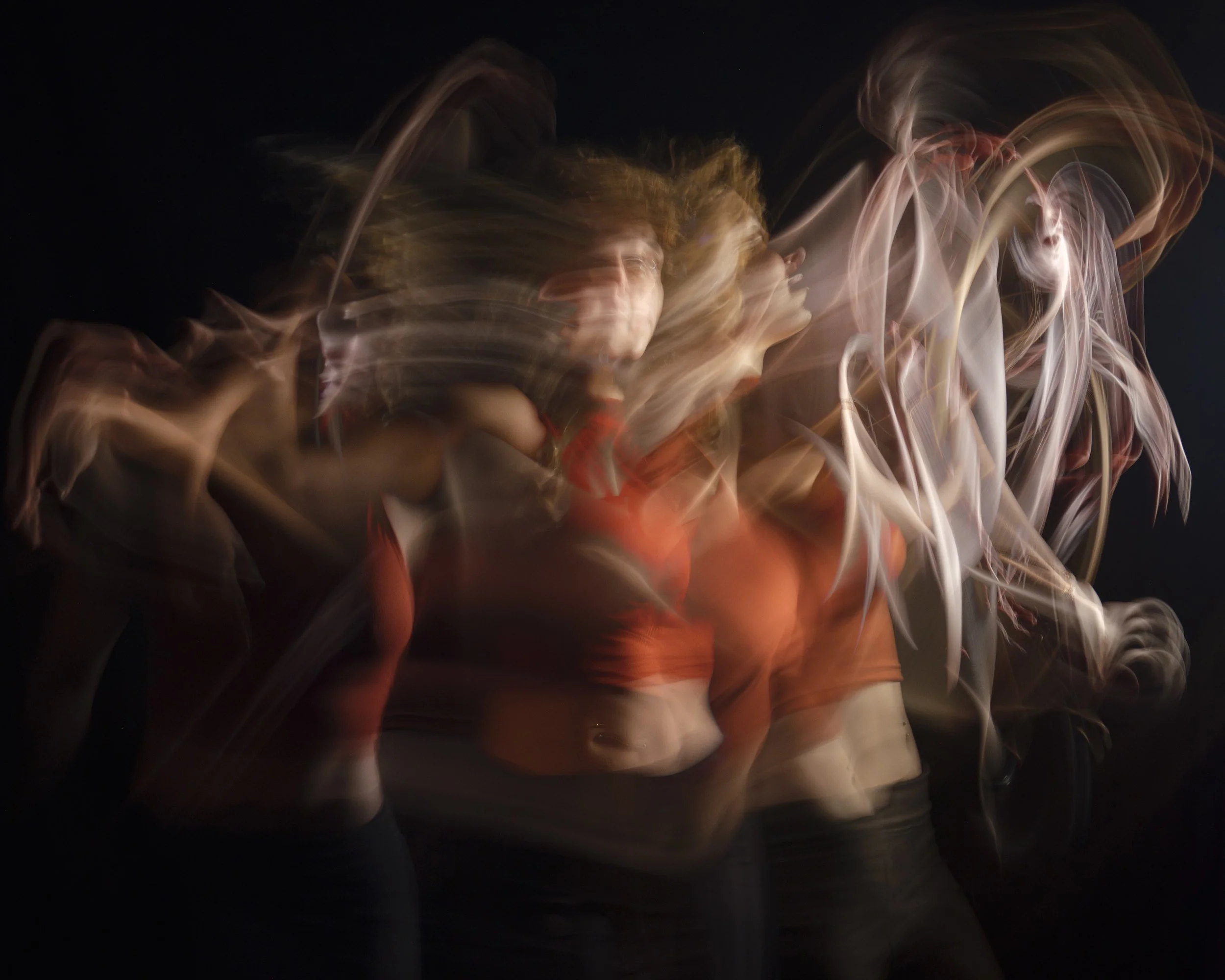 Multiple women in motion, blurred, wearing orange tops, in a dark environment with colorful light trails.