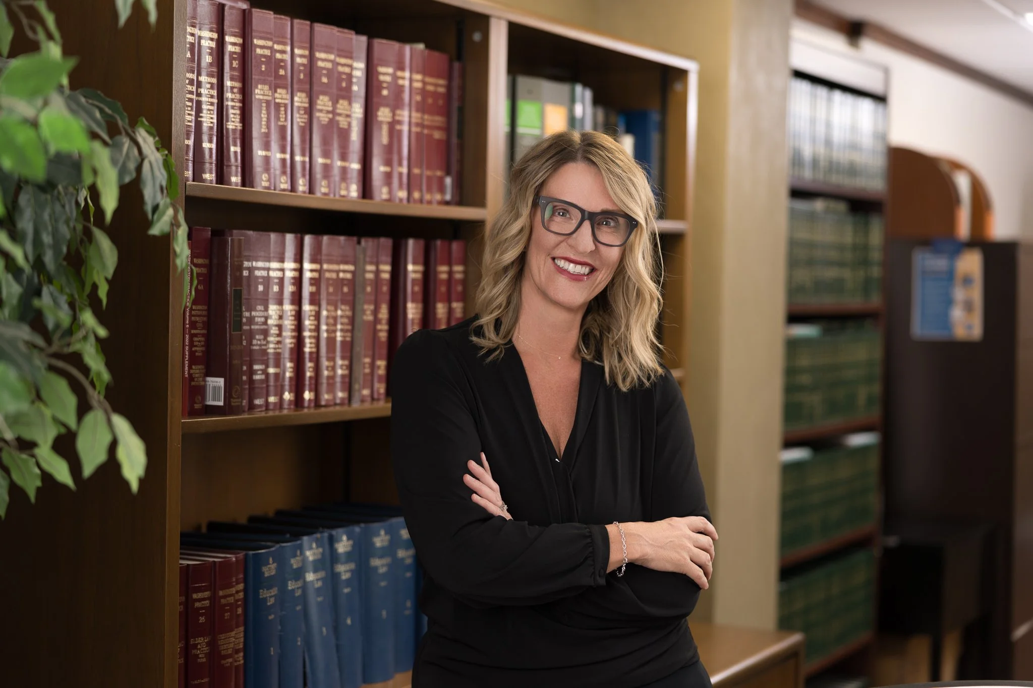 Woman in glasses smiling and standing in front of books with her arms crossed
