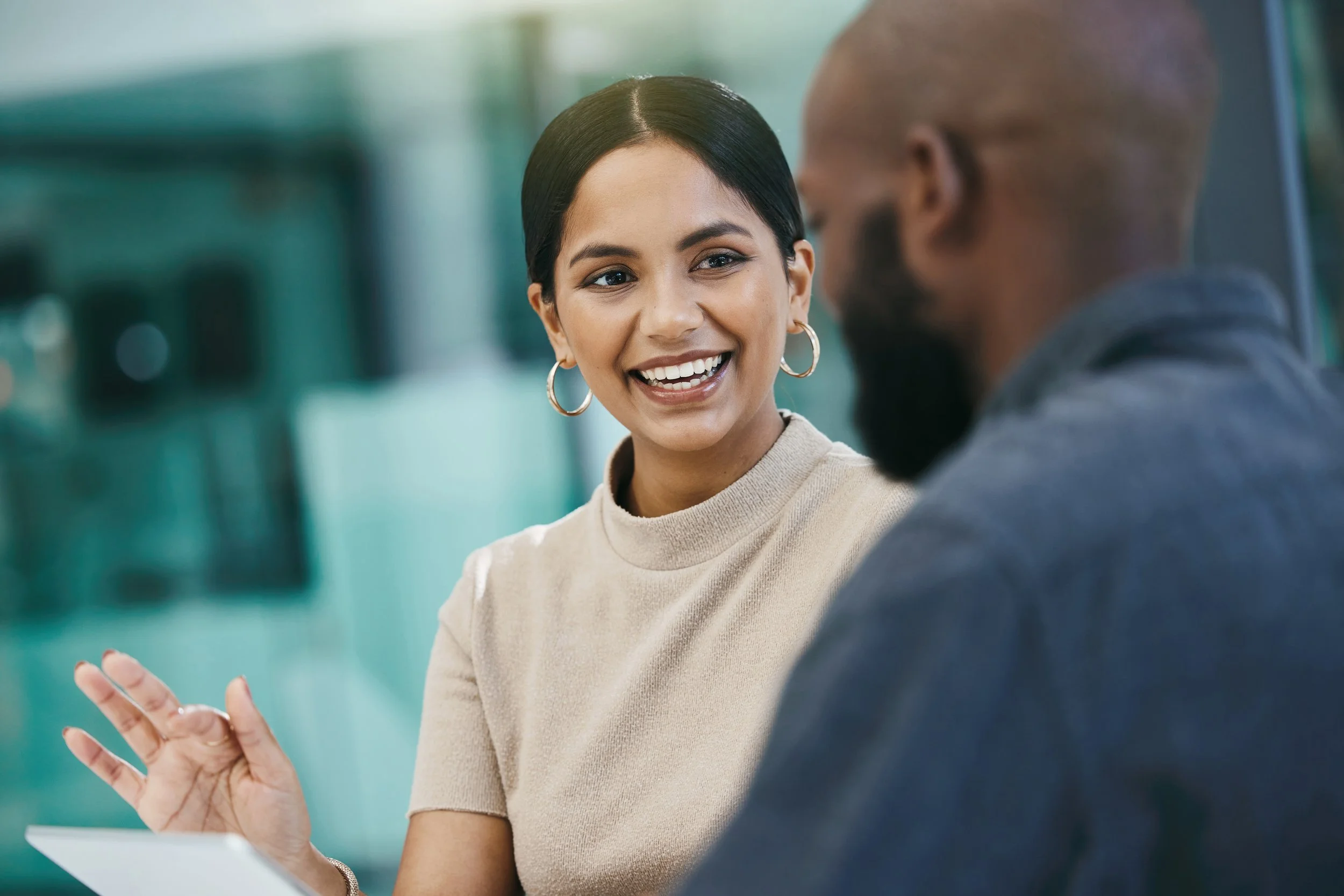 Two people having a conversation indoors, woman smiling and gesturing with her hand.