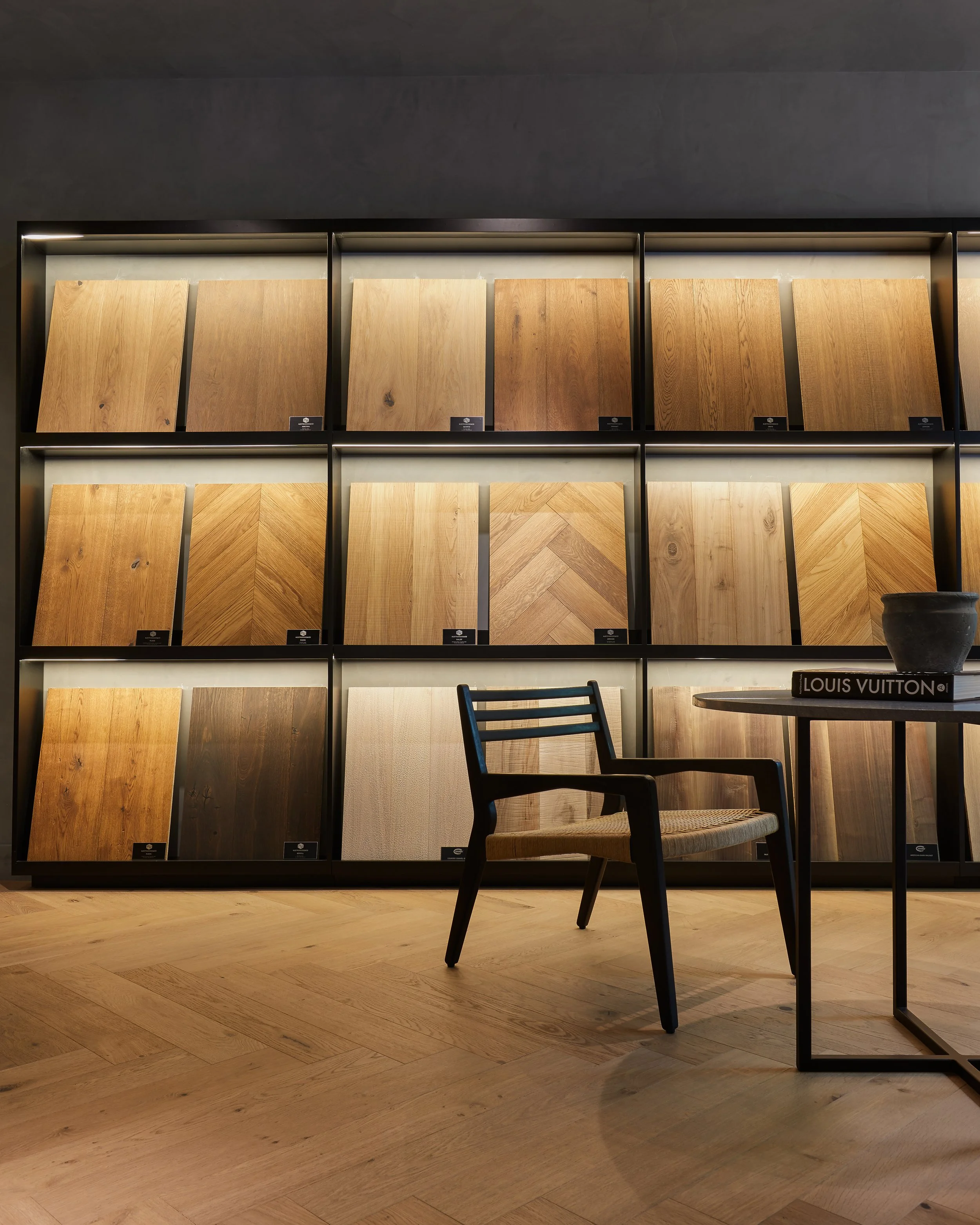 Muestras de diferentes tipos de madera en exhibición en una sala con muebles de madera y una mesa con un libro de Louis Vuitton.