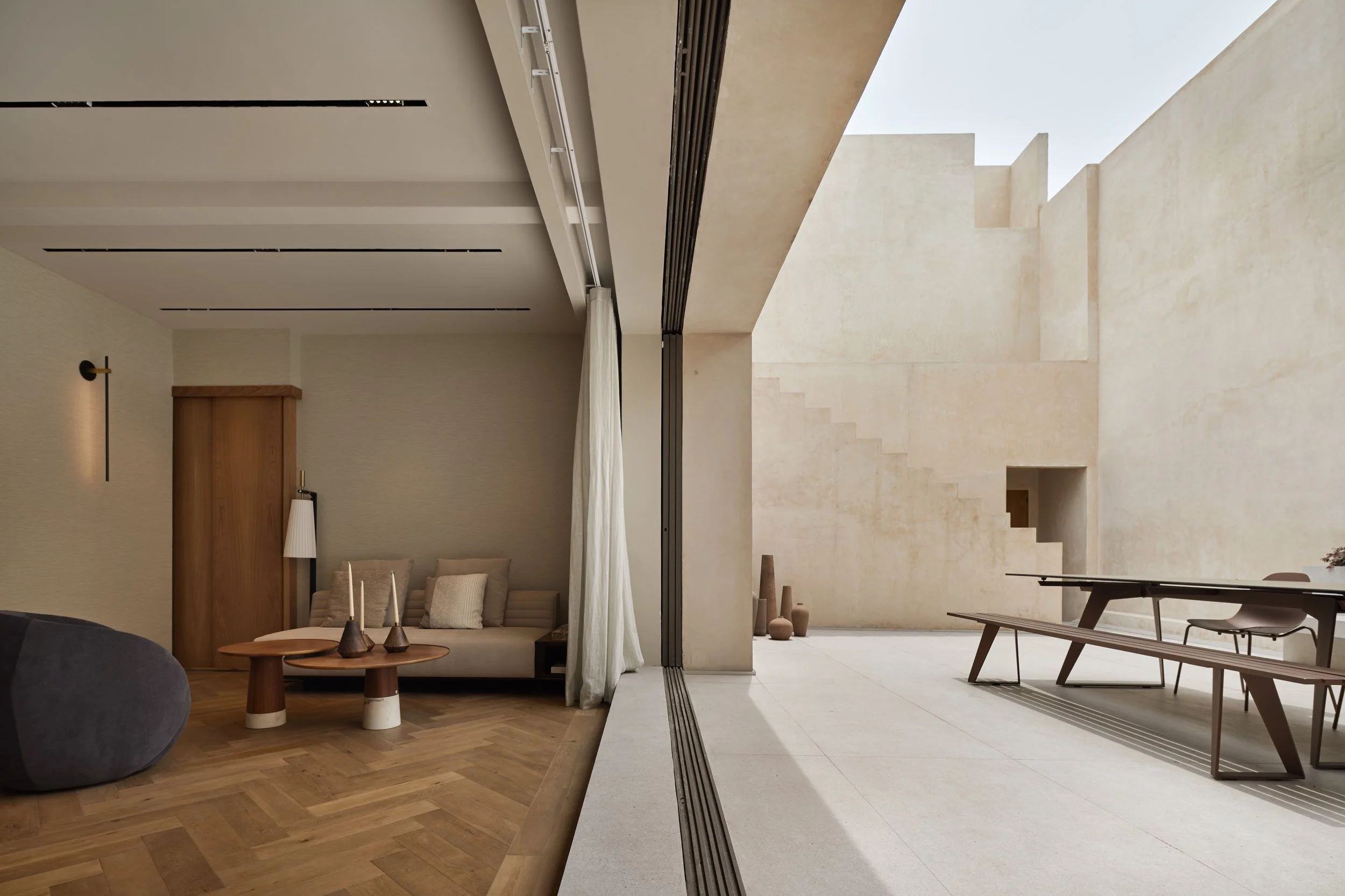 Interior de una casa moderna con paredes beige y mobiliario minimalista, que se abre a un patio exterior con escaleras y jarrones decorativos.