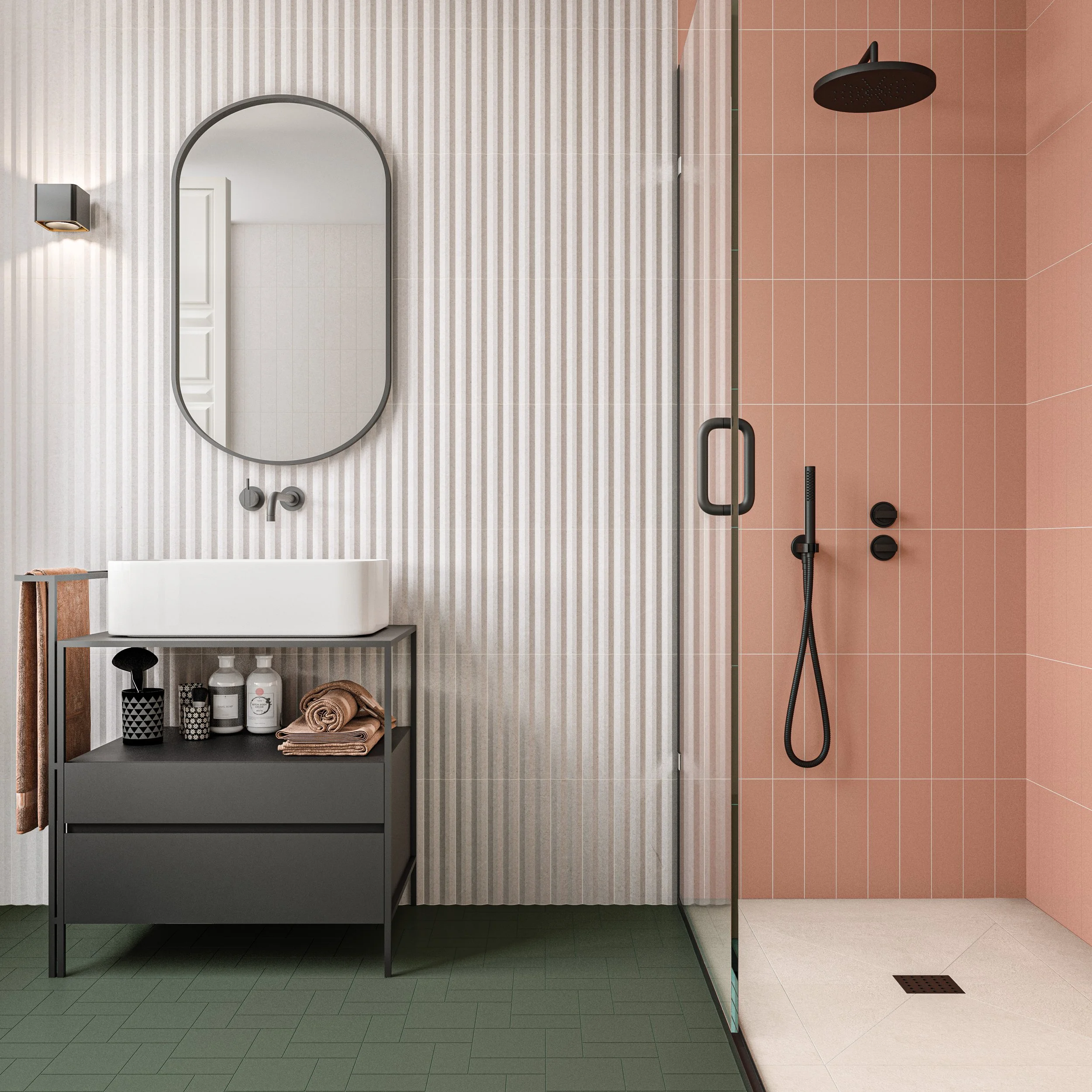 Baño moderno con pared de azulejos en tonos rosa y rayas blancas. Incluye espejos ovalados, lavabo rectangular sobre mueble gris, ducha con puerta de cristal y accesorios negros, y suelo de baldosas verdes y beige.