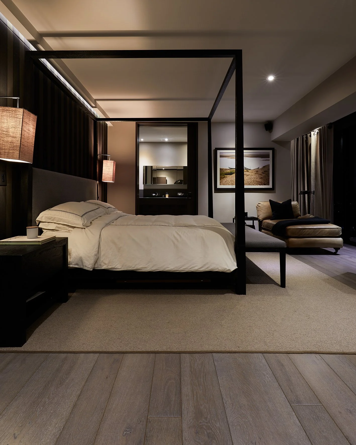 Habitación moderna con cama de cuatro postes, sillón, alfombra y decoraciones en tonos neutros.