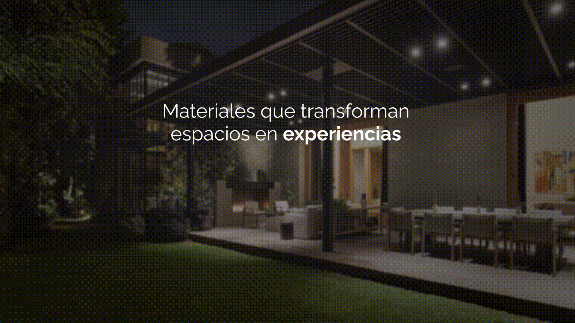 Espacio exterior de una casa moderna con sillones, mesa y chimenea, iluminado con luces, durante la noche.