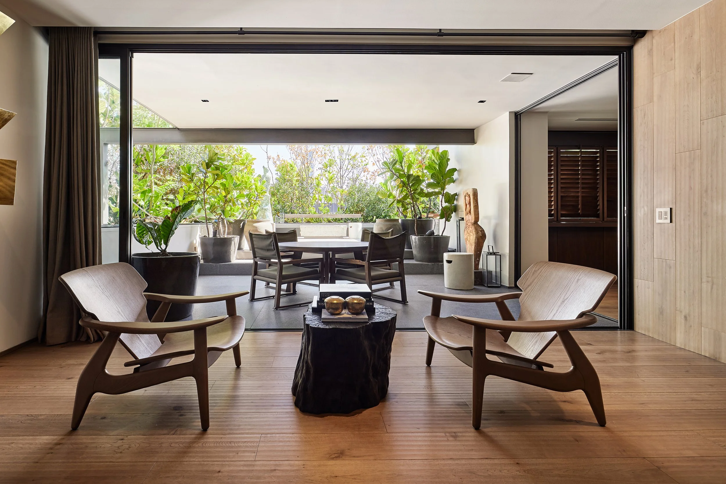 Sala de estar con vista a balcón con plantas y mobiliario moderno de madera y cojines suaves.