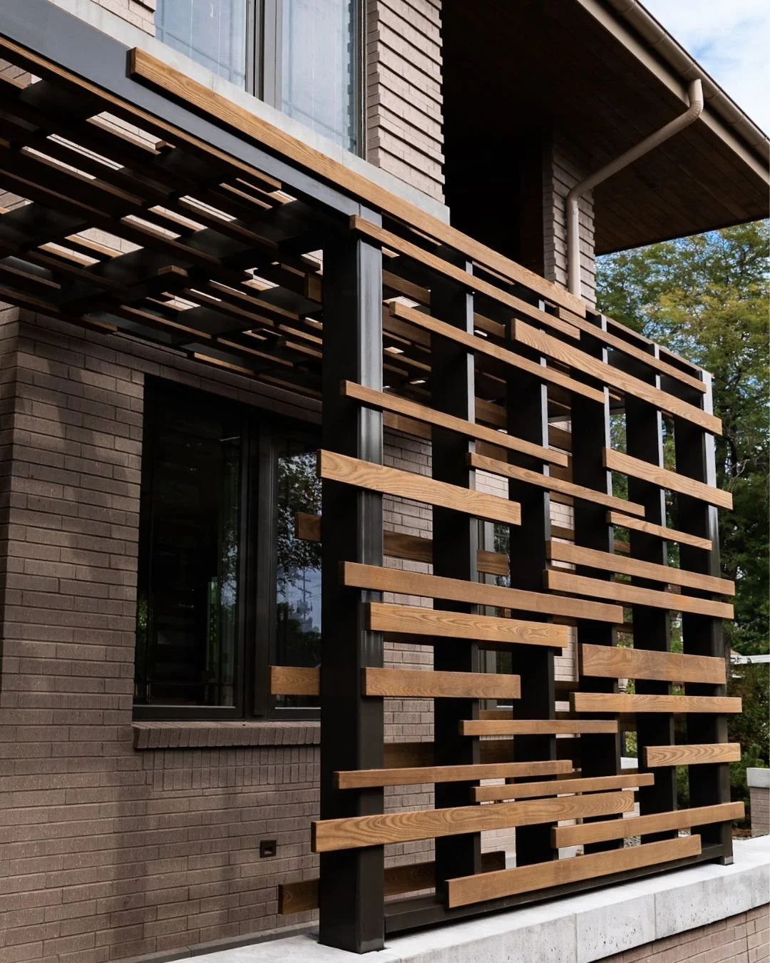 Estructura decorativa de madera y metal en la fachada de un edificio residencial de ladrillo con ventana.