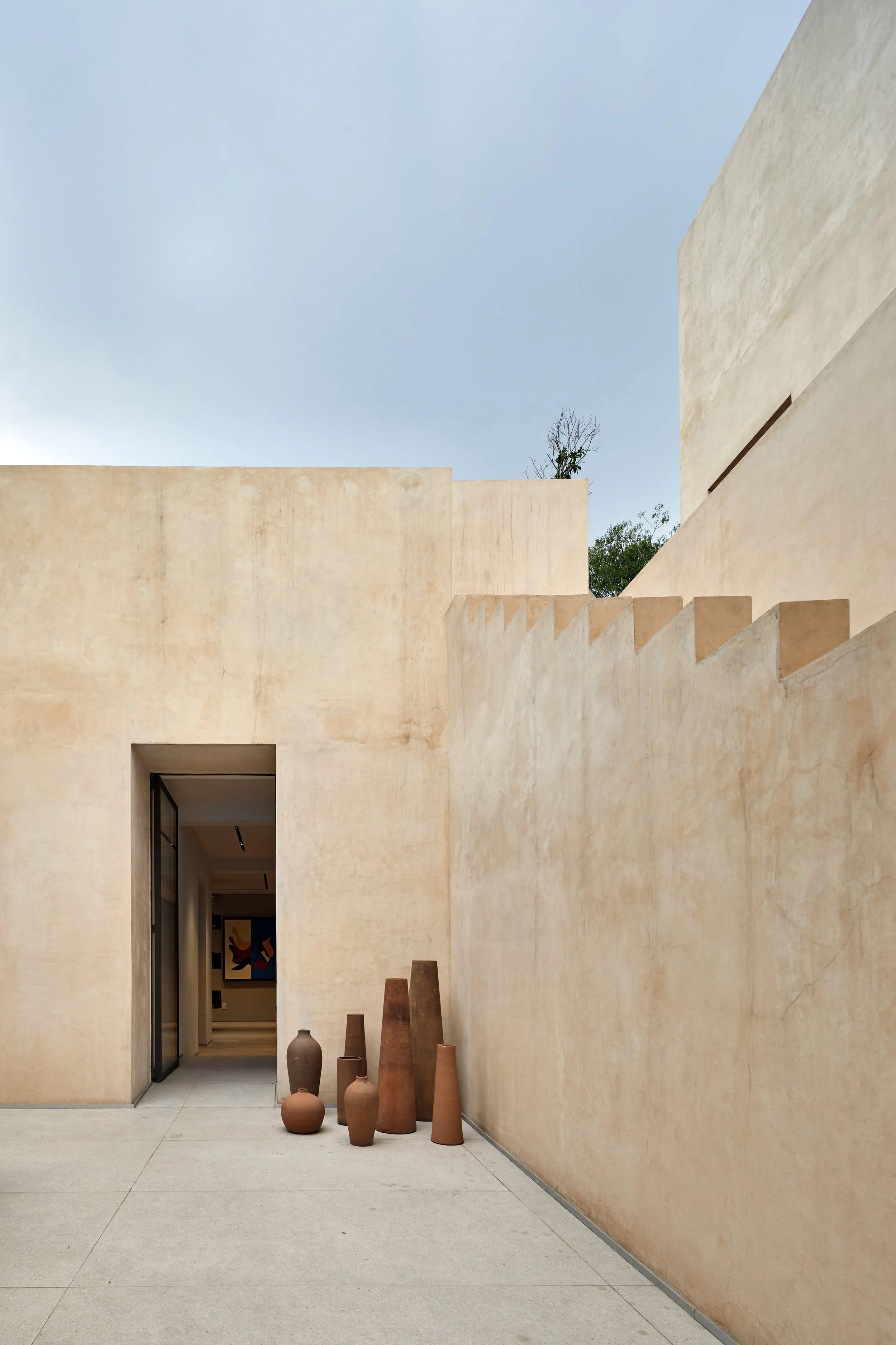 Vestidores y paredes de un edificio con tonos arena, con varias vasijas de cerámica en el suelo y un cielo nublado arriba.