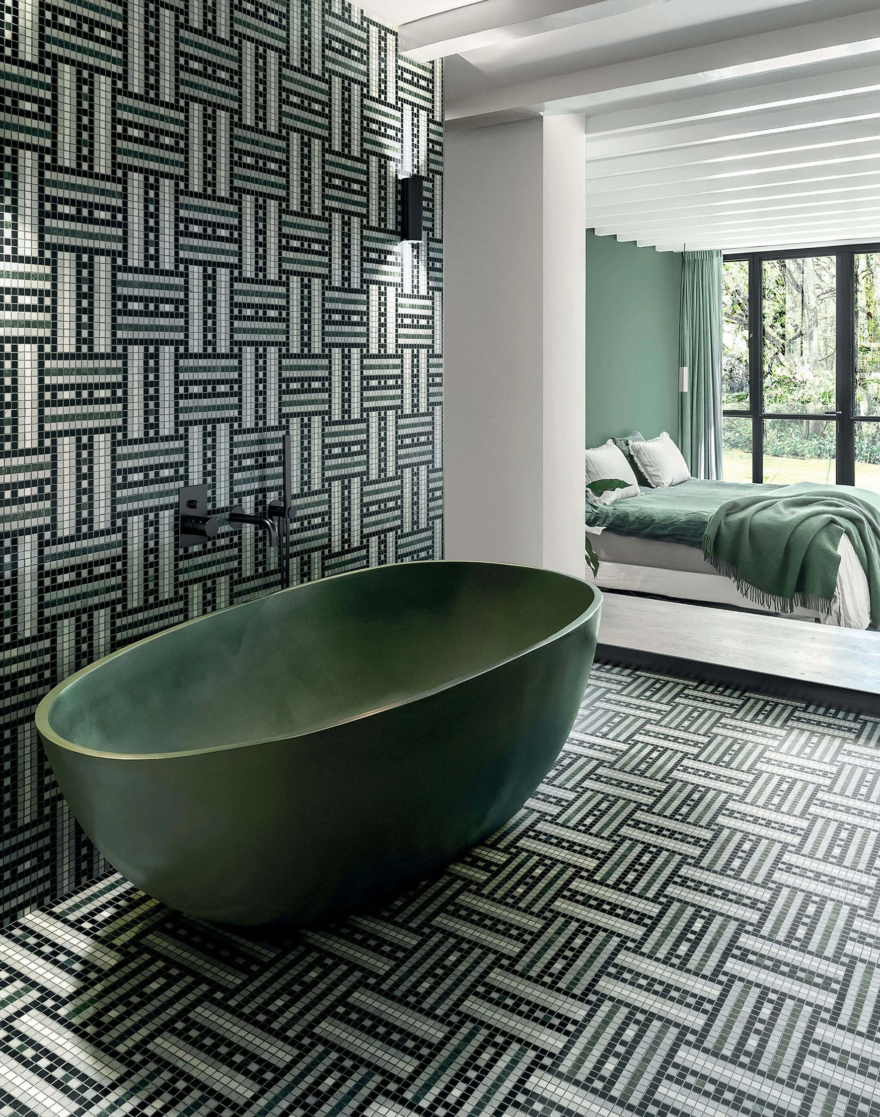 Baño con bañera verde oscuro, paredes y piso con azulejos con patrón geométrico en blanco y negro, habitación con cama con sábanas verdes y gran ventana con cortinas verdes, vistas de un jardín exterior.
