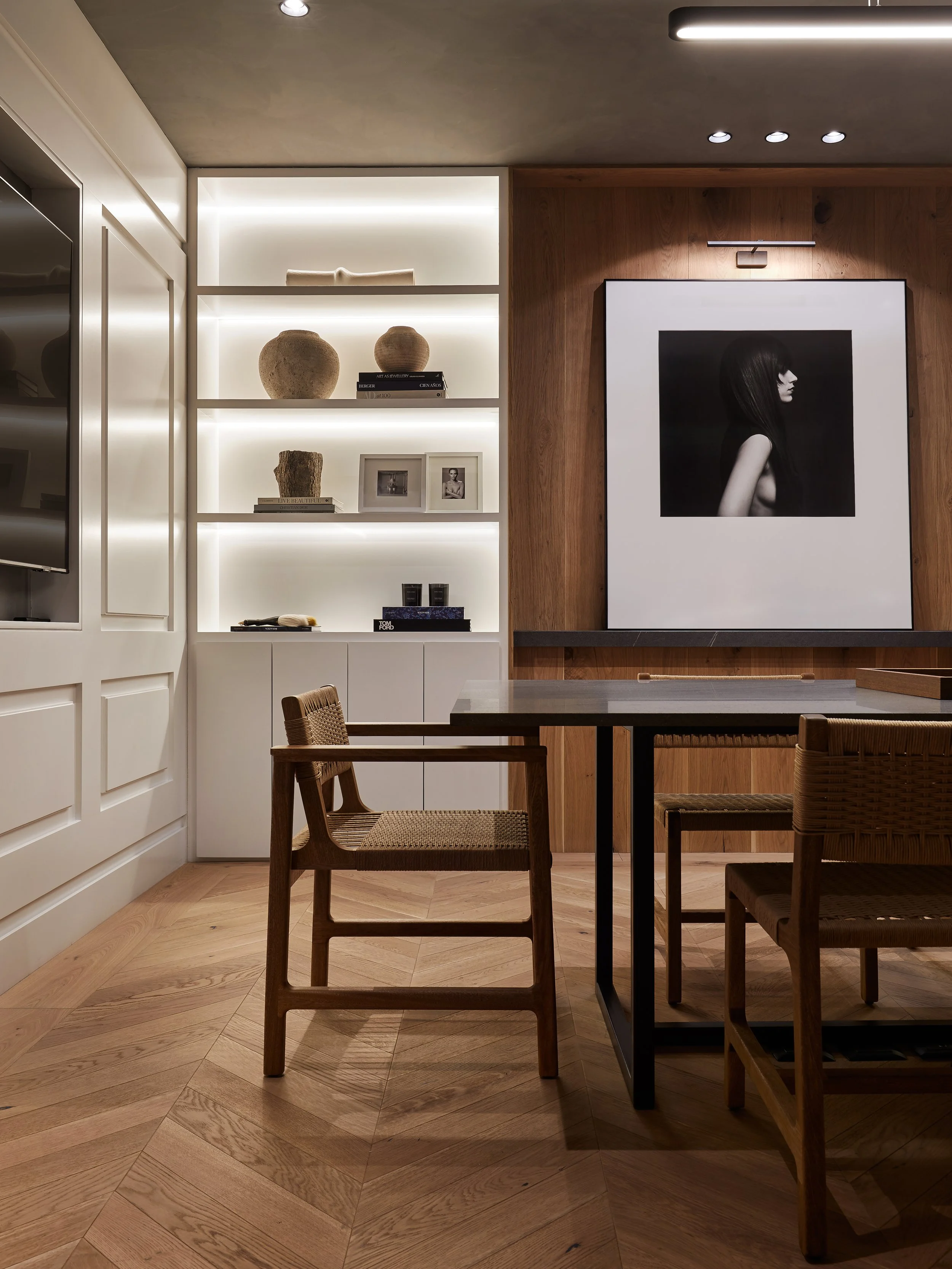 Sala de estar moderna con mesa de madera y sillas, estantería con objetos decorativos y fotografías, y una gran pintura en la pared.