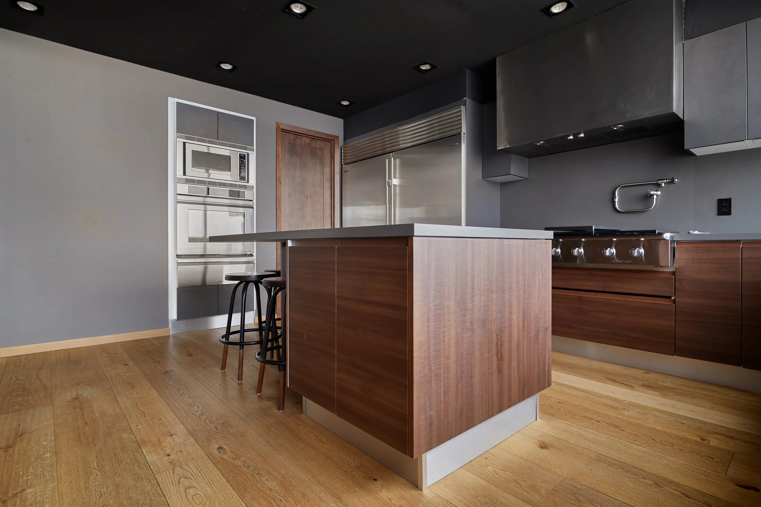 Cocina moderna con isla de madera y fregadero en la pared, electrodomésticos de acero inoxidable, paredes grises y suelo de madera clara.